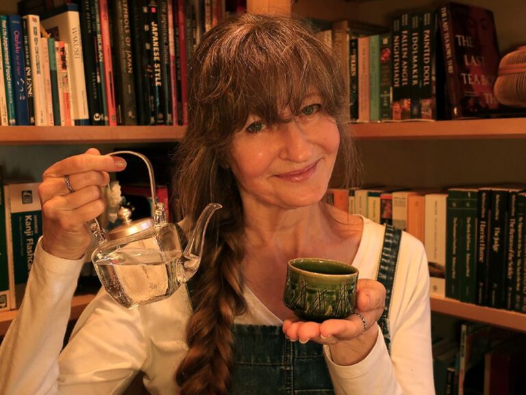 Author Jonelle Patrick stands in front a bookcase with a small teapot and cup