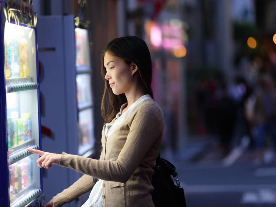 Woman wearing a white shirt and beige cardigan buying drink from a vending machine in Japan