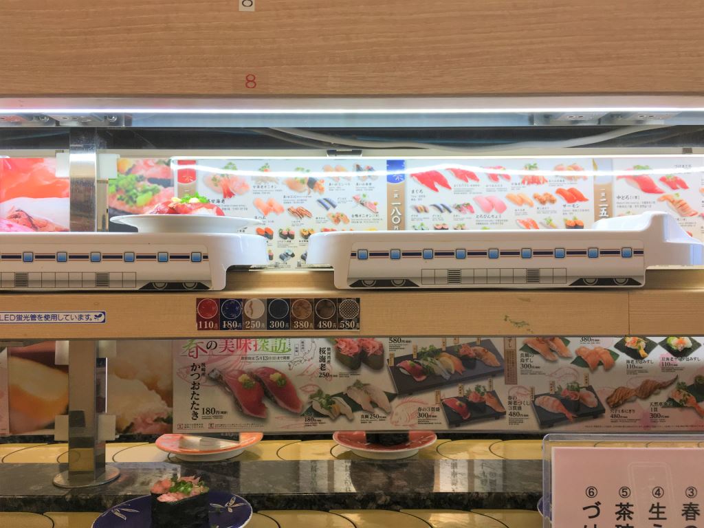 Sushi restaurant in Tokyo. A place of sushi is being delivered to a customer on a white tray that's shaped like a shinkansen train.