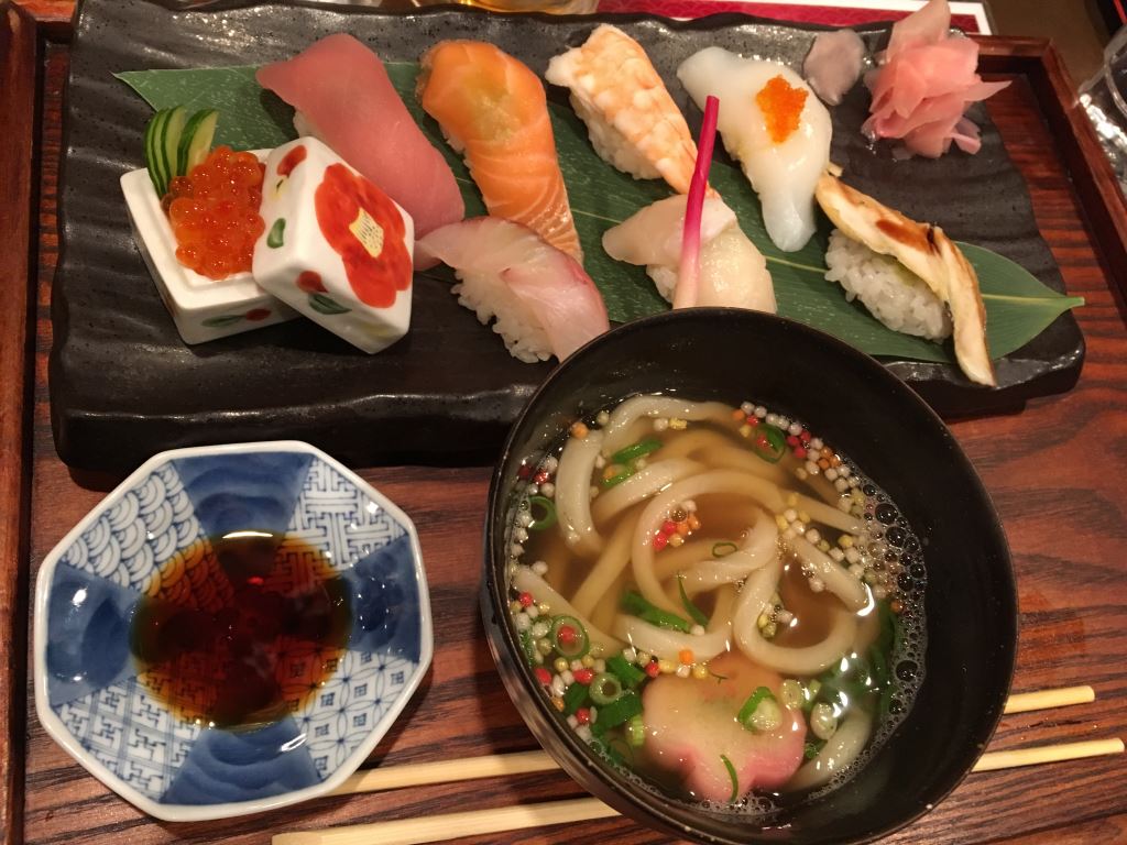 A traditional Japanese meal. There's a selection of sushi include salmon, tuna, prawn and sea bream. There's also a small bowl of udon noodles in soup and some soy sauce for dipping