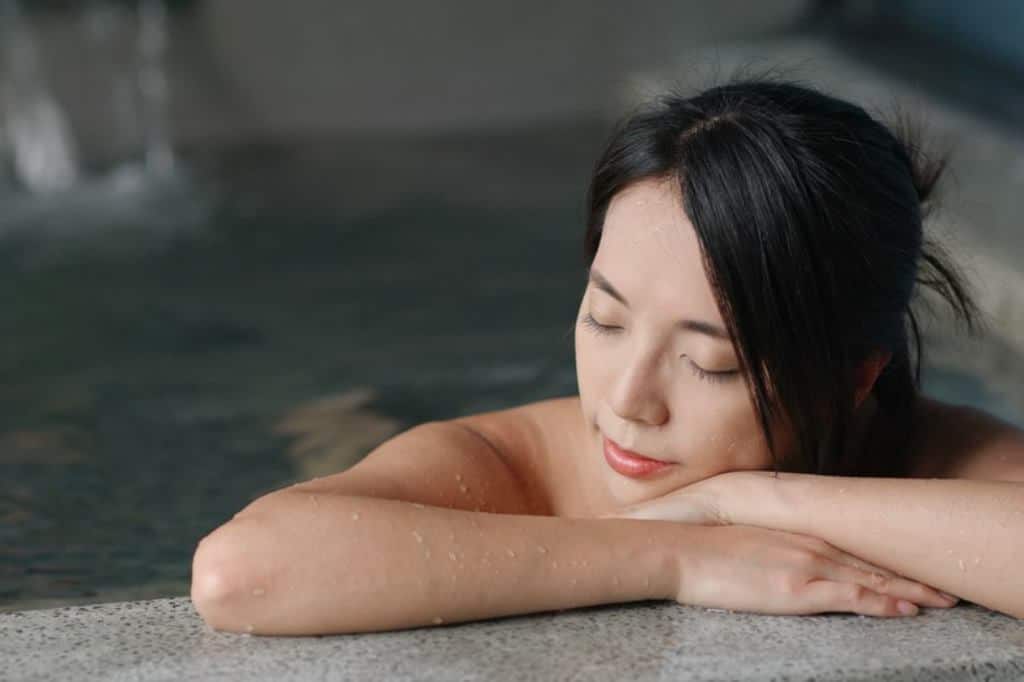 Dark haired woman rests on the edge of a hot water bath