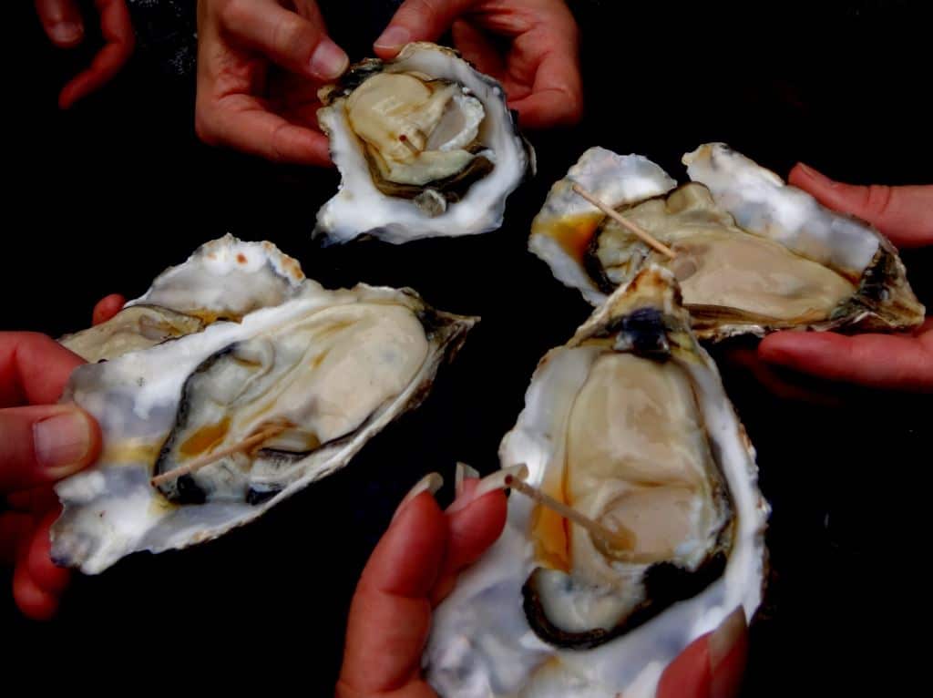 Hands hold four giant oysters ready to eat them at Tsukiji Outer Market in Tokyo.