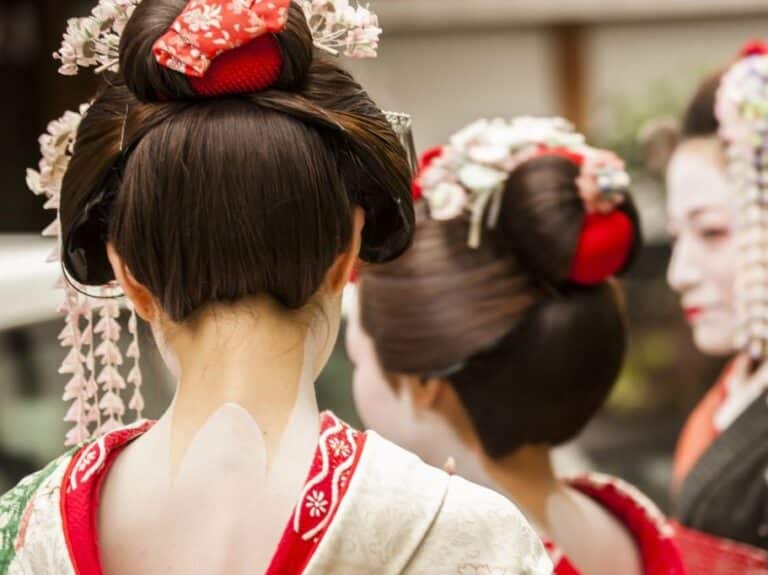 Two Maiko in Kyoto - photographed from behind. They have some skin showing under the white make up on their neck and a red collar. This shows they are Maiko, not geisha.