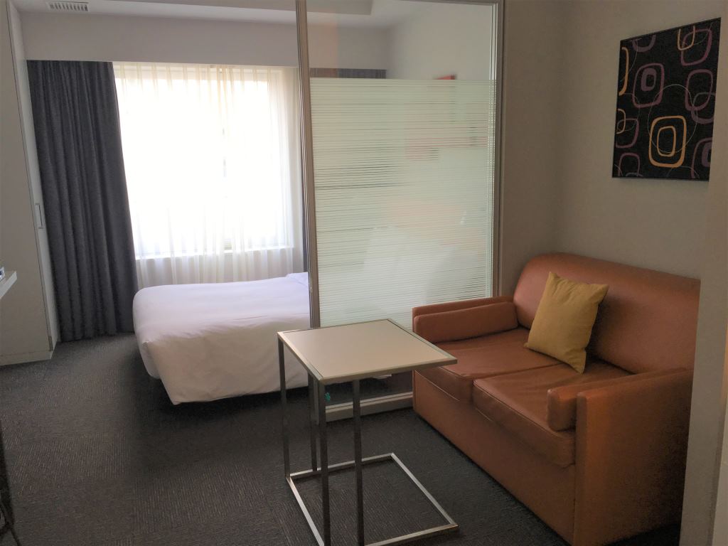 Interior of the room at Citadines Shinjuku showing a sofa, a small table and a bed. There's a desk, bathroom, vanity area and a kitchenette out of shot