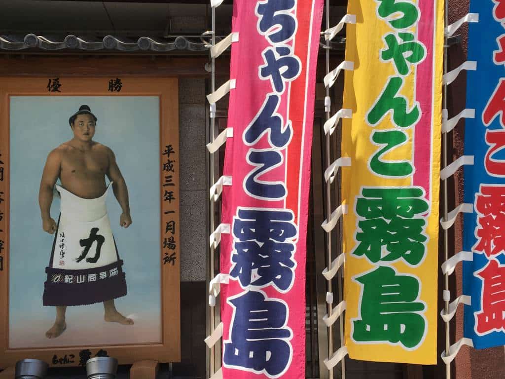 Portrait of a famous sumo wrestler outside a building in Ryoguku Japan.  Colorful sumo flags are next to the picture.