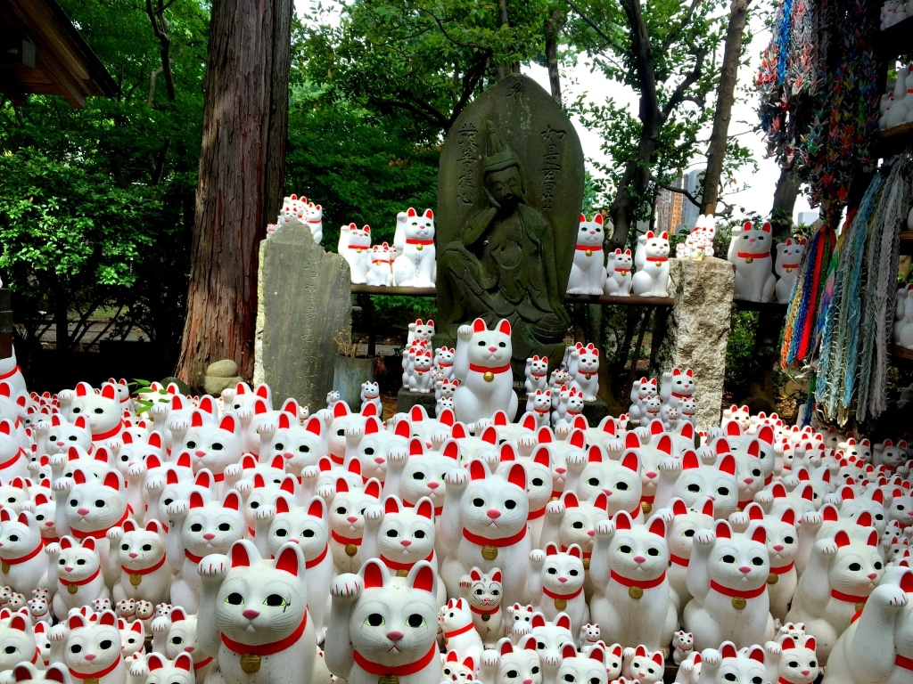 Waving cat statues in Tokyo's Gotoku-ji temple. The cats are white with red ears, red noses and red collars. They all raise their right paw in the air - there are hundreds of them in the picture of all different sizes, but all in the same position.