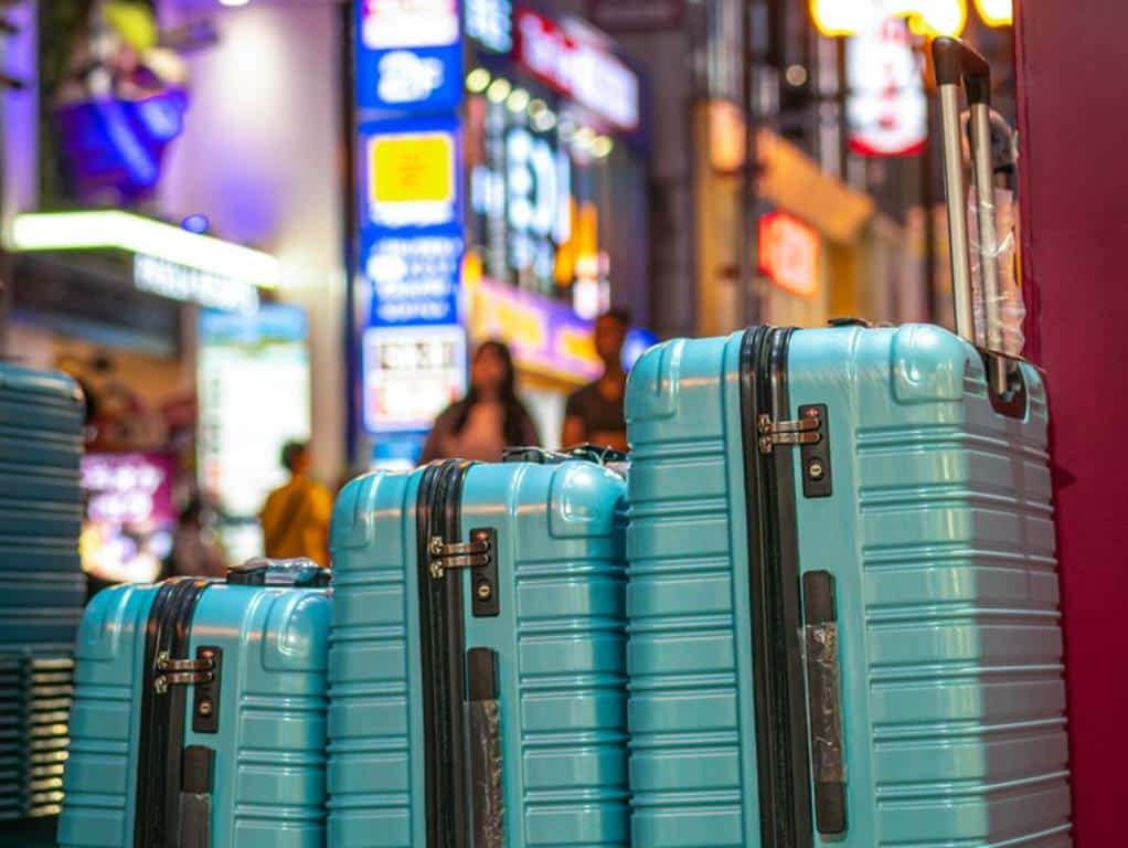 Row of green suitcases photographed against neon signs in Japan
