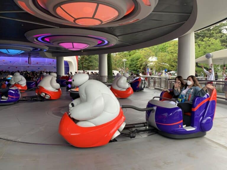 the Baymax ride at Tokyo Disneyland - a white Baxmax figure drives a red car pulling a purple car with people in