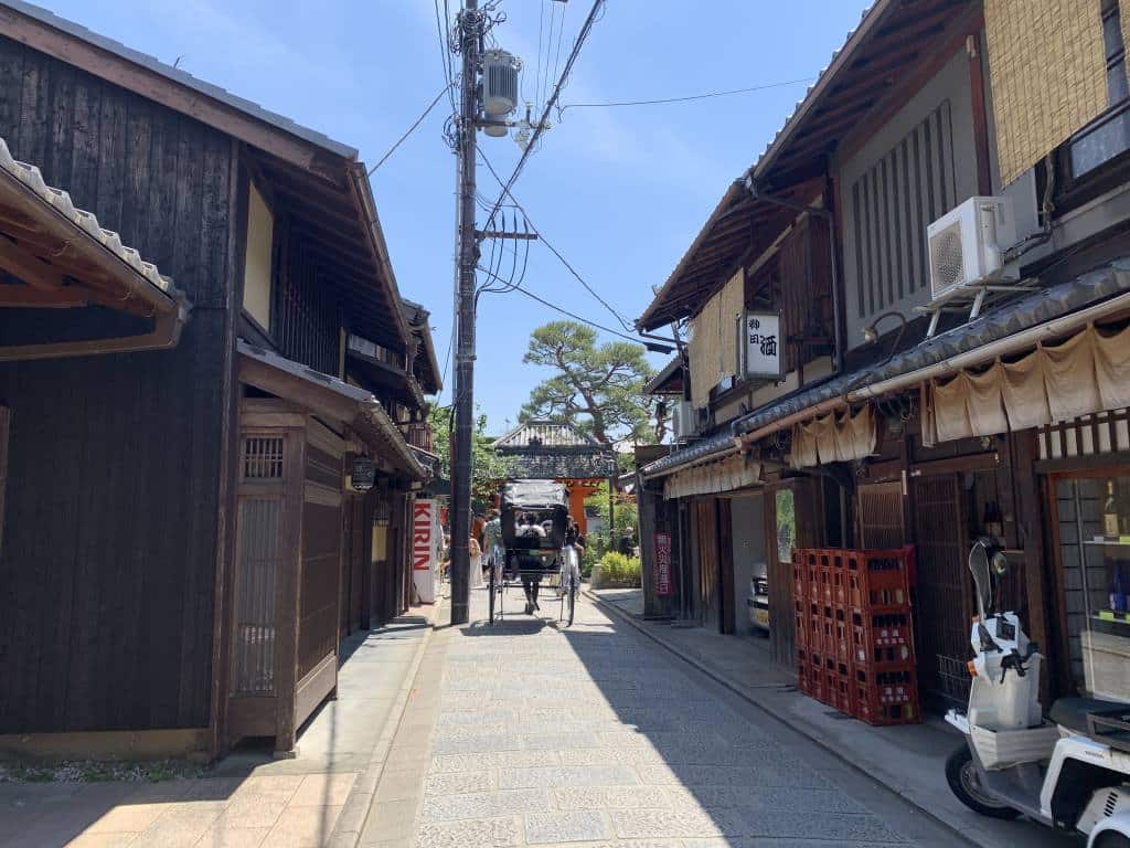 A quiet alley in Kyoto lined with bars. There's a ricksaw taking tourists on a tour in the distance.