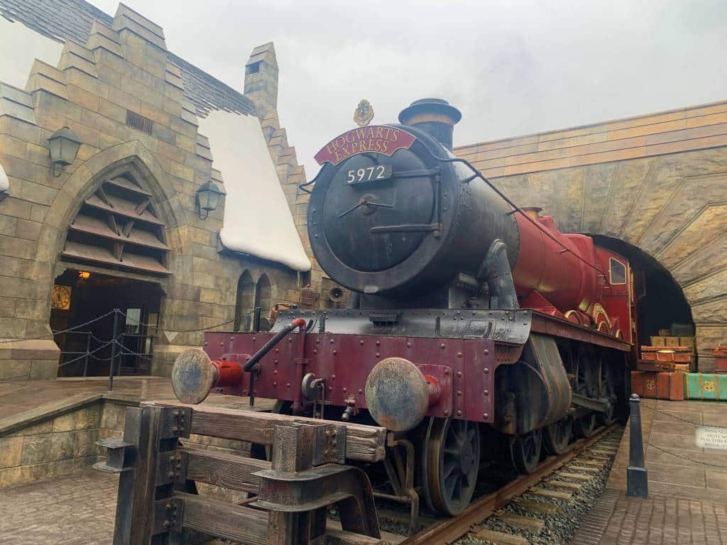 The Hogwarts Express Steam train at Universal Studios Japan. It's a black and red train with steam coming out of the chimney - a pile of suitcases is stacked on the platform beside it