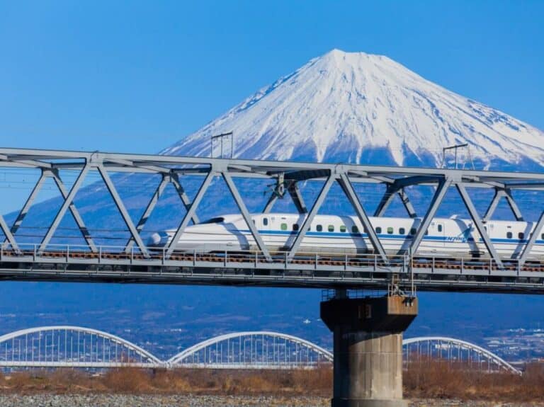 Shinkansen train traveling over a bridge with Mount Fuji in the background