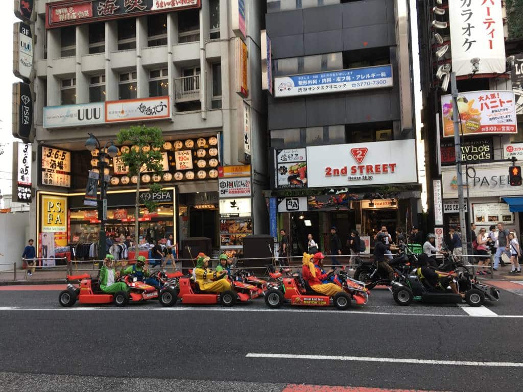A queue of Go Karts being driven by people in costume sit at a traffic light in Shibuya Japan