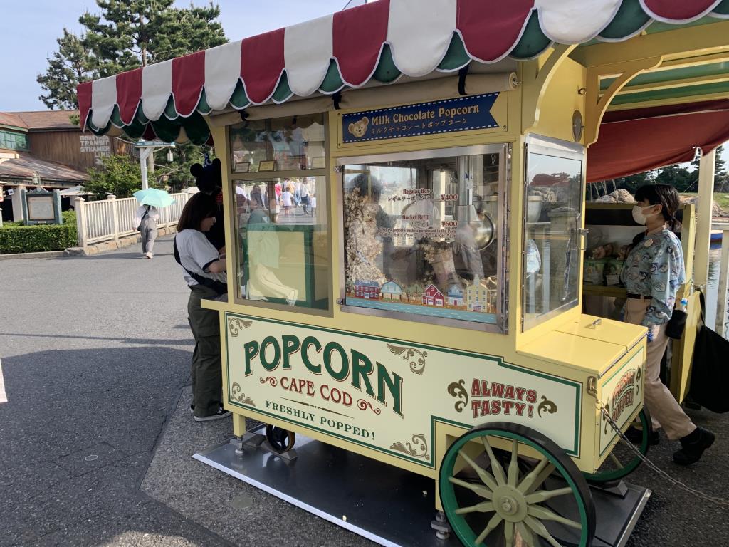 Popcorn cart in Tokyo DisneySea. It's a yellow cart with a red and white striped roof - the sign on the side says Popcorn Cape Cod. It's selling Milk Chocolate Flavour