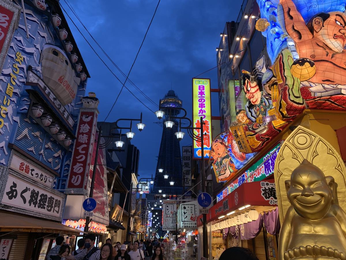 Nighttime view of Shinsekai in Osaka showing a gold billiken, neon signs and the Tsukentatsu tower in the background