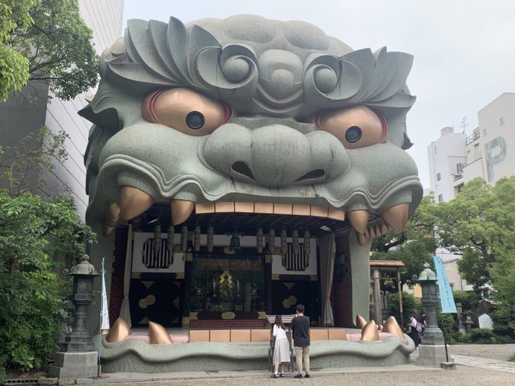 Giant lion head at Namba Yasaka Shrine in Osaka where we start our three day Osaka itinerary. A couple stand in front of the lion's mouth  - they only come up to it's lower teeth.