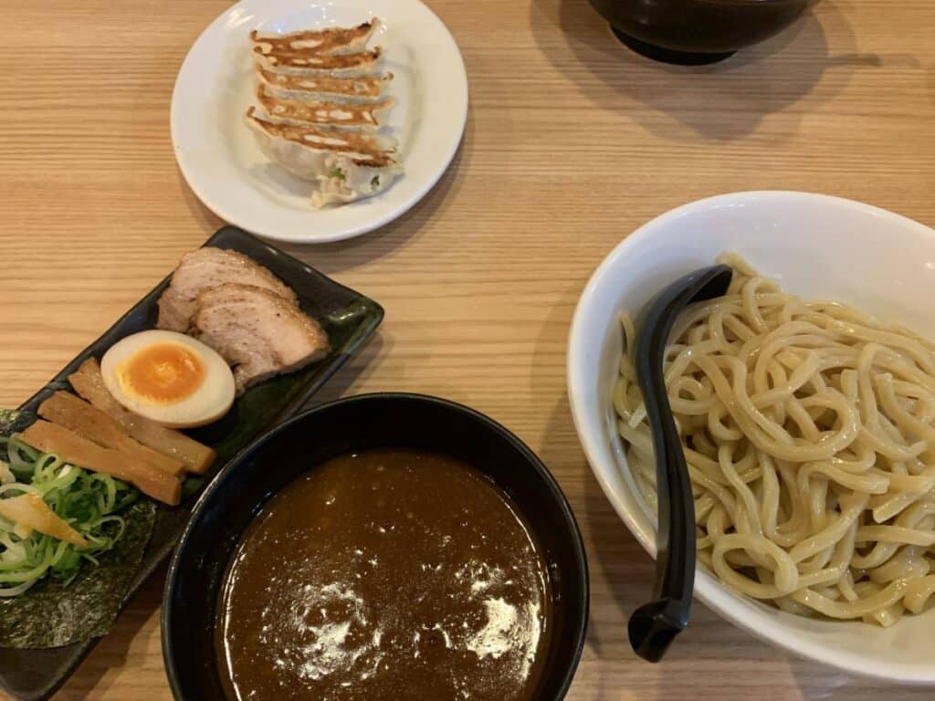 Plate of soba noodles with a dipping sauce, slices of pork, half an egg and vegetables. With a side of gyoza