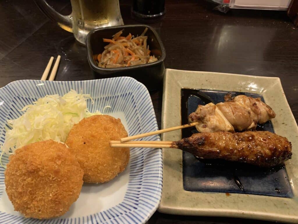 Plate of yakatori style food in tokyo. There's a skewer or grilled chicken, a chicken meat ball and some crab croquettes