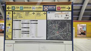 Sign at Tokyo's Shibuya Station showing all the exits. A metro train sits behind it with the doors open.