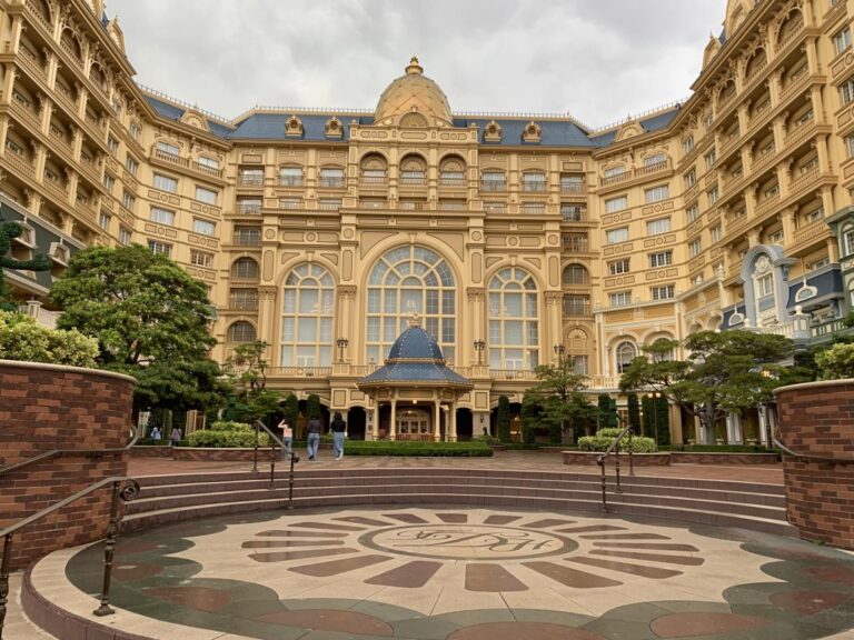 Exterior of the Tokyo Disneyland hotel. It's a gold coloured building with huge picture windows. Rooms surround a U shaped courtyard, some have balconies.