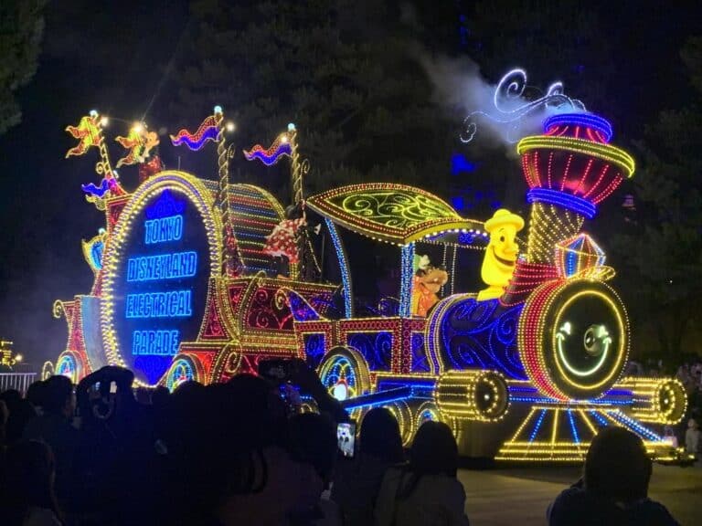 Float in the Tokyo Disneyland Electrical Parade - it's covered in yellow, red and blue lights and Goofy waves from the float.
