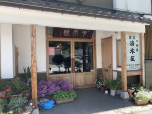 Outside view of the Shimuzuya Ryokan in Nagano. It has a wood and glass door and lots of pots of flowers and other plants outside.