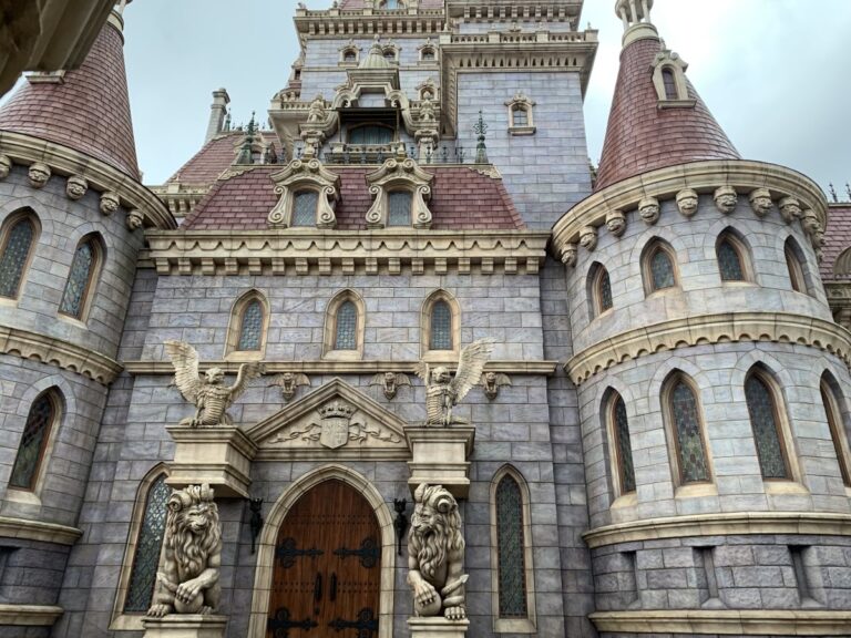 Exterior of Beast's castle in Tokyo Disneyland. Giant lions flank a wooden door. The castle is built of grey stone blocks