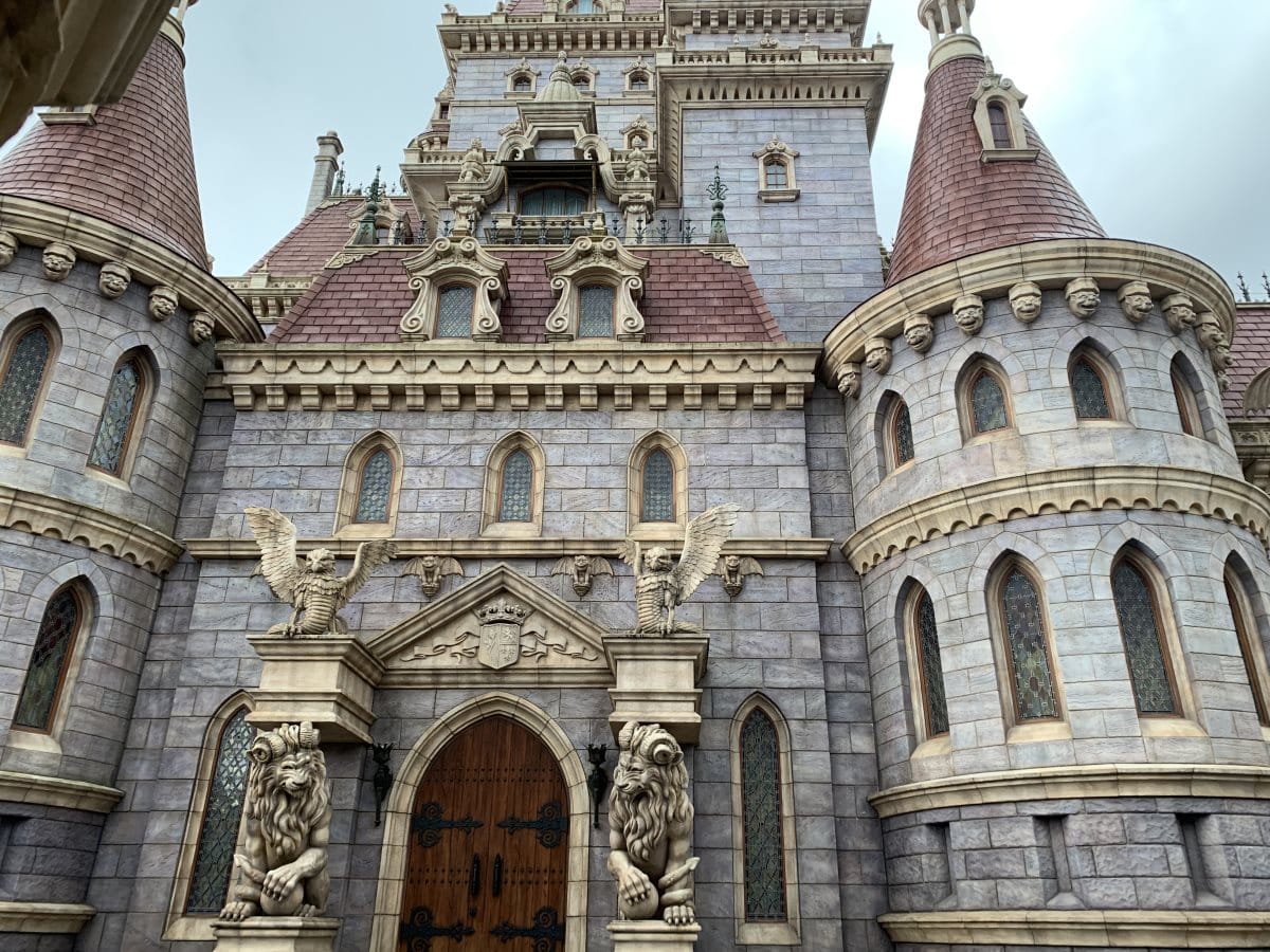 Exterior of Beast's castle in Tokyo Disneyland. Giant lions flank a wooden door. The castle is built of grey stone blocks