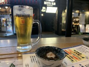 a glass of beer and a small bowl of otoshi on a table in a bar in Sendai, Japan