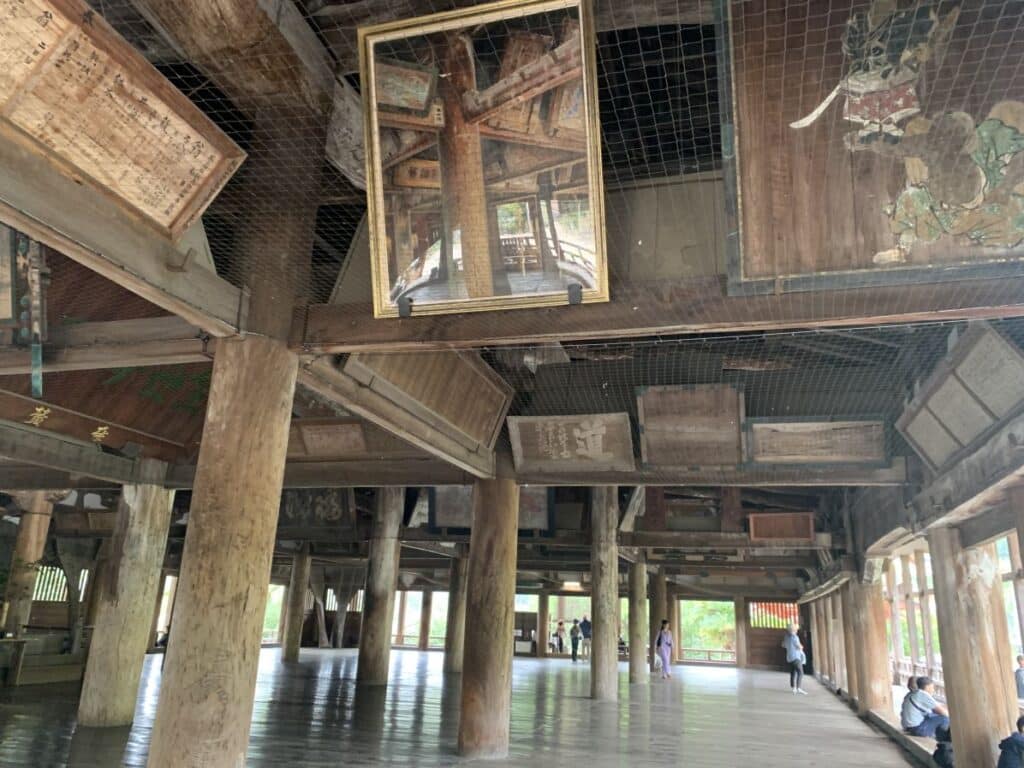 Inside Hokoku Shrine in Miyajima showing the wooden floor, thick wooden columns and art works arranged around the roog