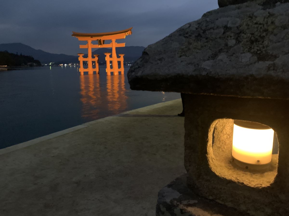 View of the red torii gate in Miyajima at night. It's illuminated so glows above the black water