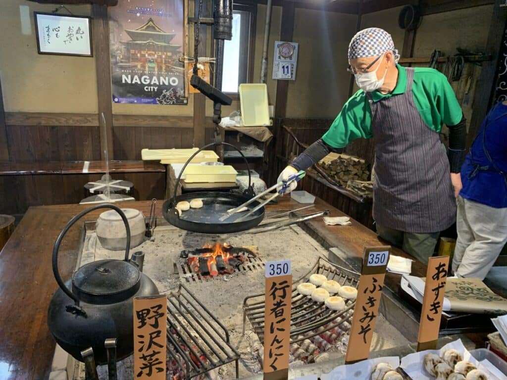 Man in an apron and head scarf cooks oyaki dumplings over a open fire in Nagano