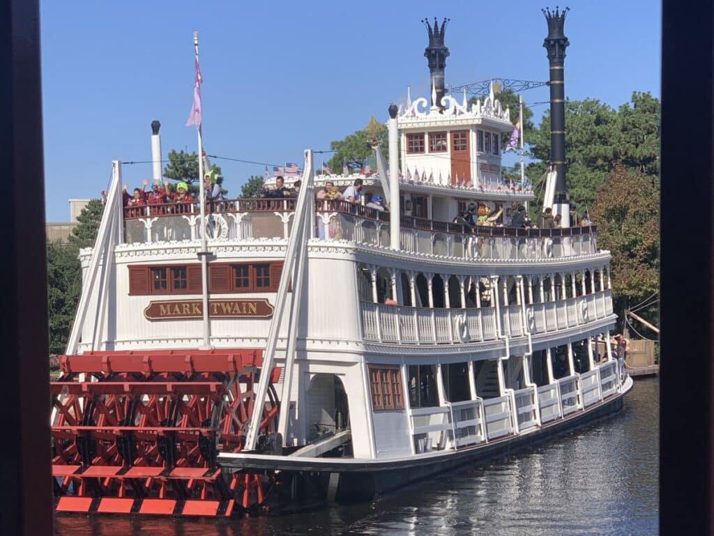 Mark Twain Riverboat at Tokyo Disneyland - it is a paddlesteamer with a red paddle at the back and white lattice balconies along the side