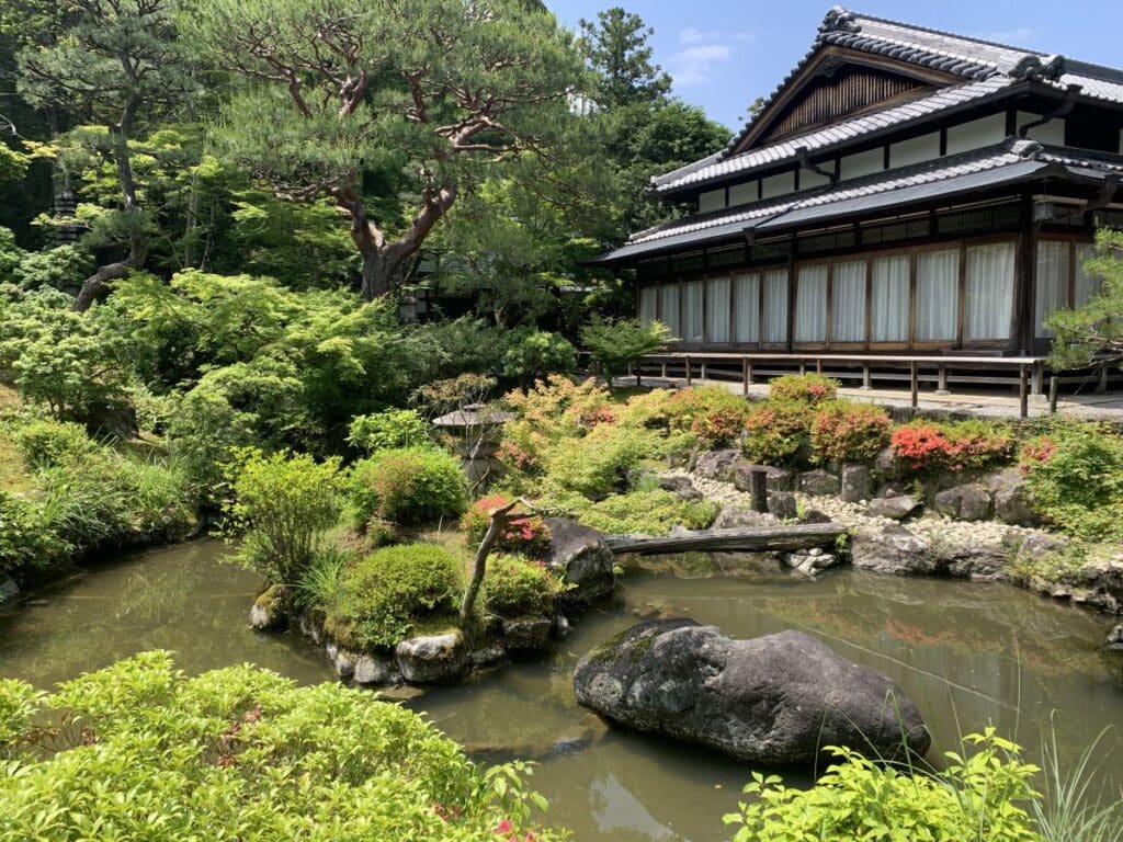 View of a pond, trees and a wooden building in Yoshikien Garden, Nara