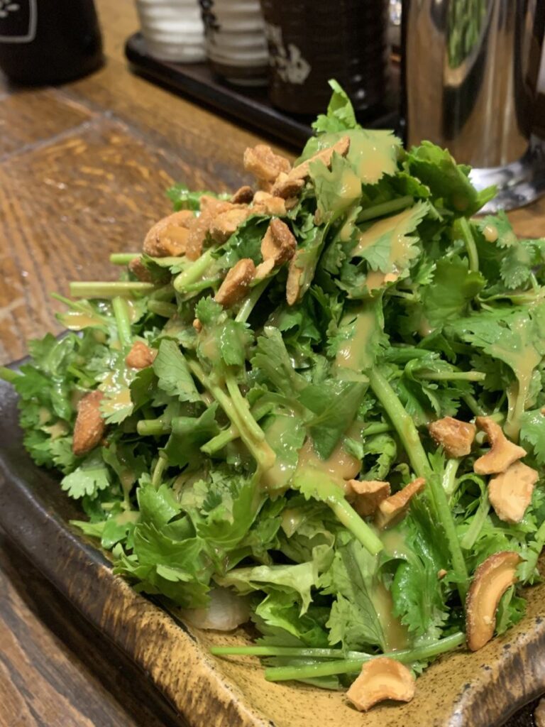 Plate piled high with coriander topped with cashews and dressing