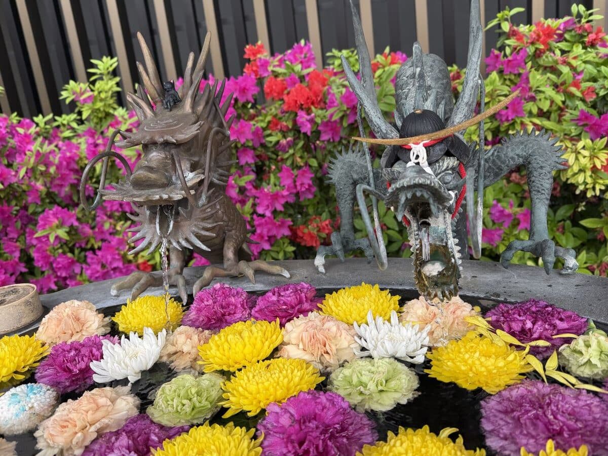 Two dragons deliver water to a flower filled purification trough in Japan. One of them has a tiny cat sitting on his head - the other wears a small samurai helmet.