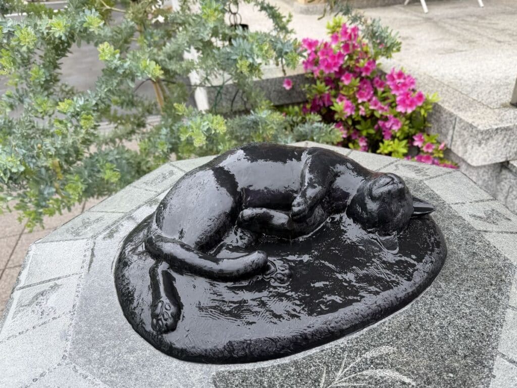 Another statue of a black cat at Komagome Shrine - this one is lying down.