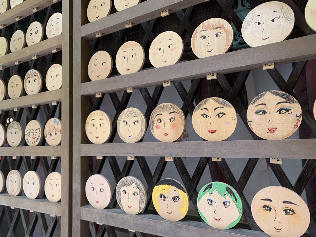 Prayer plaques shaped like mirrors with faces drawn on them at the Kawai shrine in Kyoto