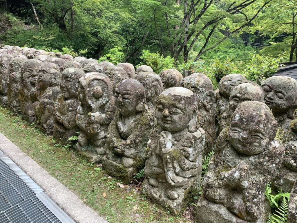 Stone figures covered in moss with carved faces at Otagi-Nenbutsu-ji in Kyoto. One carrries a tennis racket and ball.