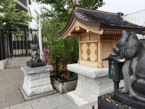 cat statues flank a small wooden shrine at Komagome Shrine in Tokyo