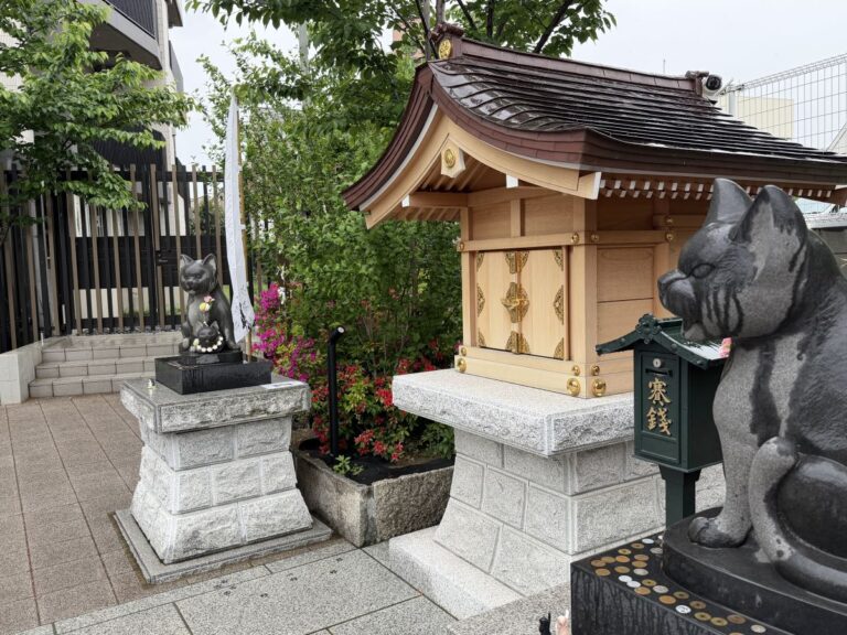 cat statues flank a small wooden shrine at Komagome Shrine in Tokyo