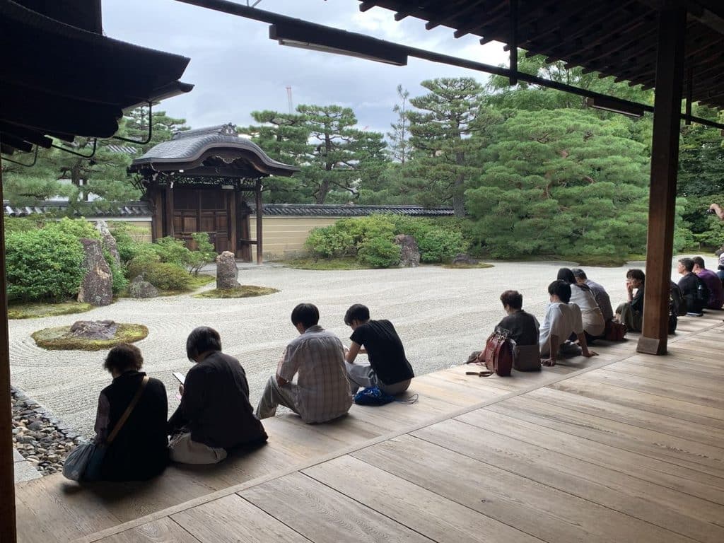 People sit on the edge of the deck at Kennin ji looking at the gravel zen garden