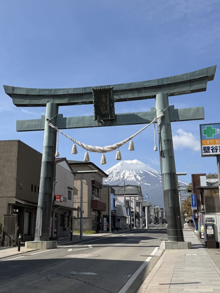 A faded green torii gate sits at the end of a road with Mount Fuji framed behind it. 