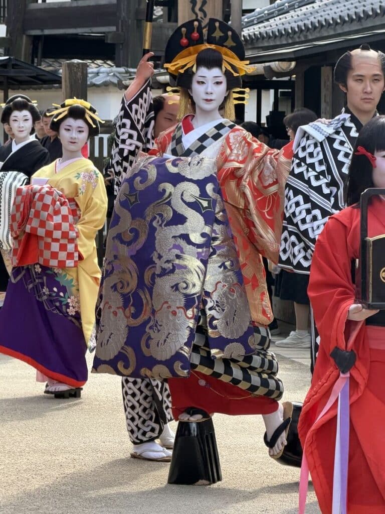 White faced oiran in an elaborate gold and red kimino with a purple and gold obi walks at Edo Wonderland in Nikko